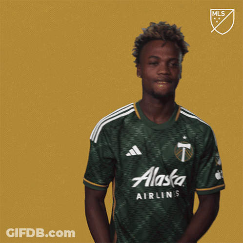 A Man Wearing A Green Alaska Shirt Stands In Front Of A Gold Background GIF