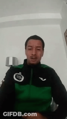 A Man Wearing A Green And Black Jacket Is Making A Face . GIF