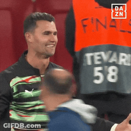 A Man Wearing A Green And Black Shirt With The Number 58 On It Is Smiling . GIF