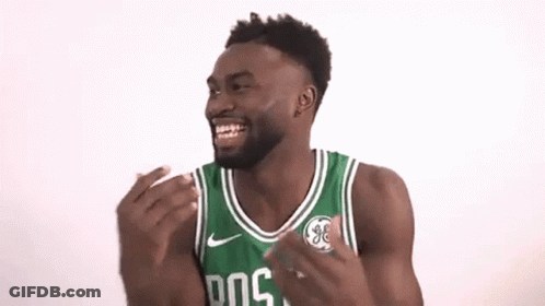 A Man Wearing A Green And White Boston Celtics Jersey Is Laughing With His Hands In The Air . GIF