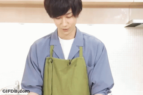 A Man Wearing A Green Apron And A Blue Shirt Is Cooking In A Kitchen GIF