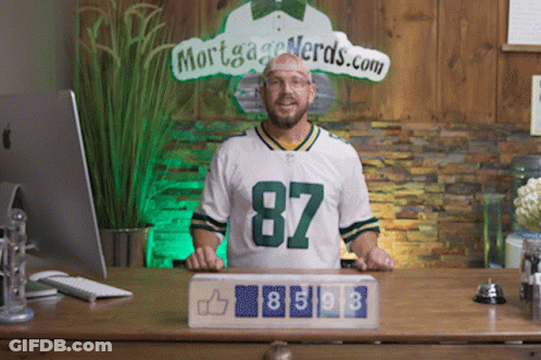 A Man Wearing A Green Bay Packers Jersey Stands In Front Of A Sign That Says Mortgage Nerds.com GIF