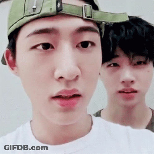 A Man Wearing A Green Hat And A White Shirt Is Standing Next To Another Man GIF