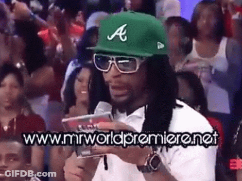 A Man Wearing A Green Hat With The Letter A On It Stands In Front Of A Crowd Of People GIF