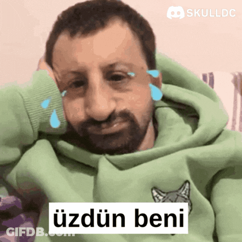 A Man Wearing A Green Hoodie Is Crying With Skulldc Written Above Him GIF