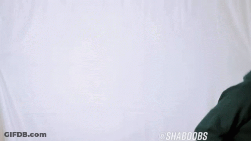 A Man Wearing A Green Hoodie Is Dancing In Front Of A White Wall . GIF