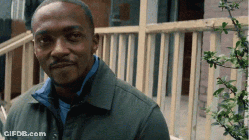A Man Wearing A Green Jacket And A Blue Shirt Is Standing In Front Of A Railing GIF
