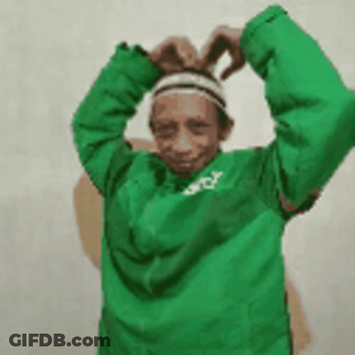 A Man Wearing A Green Jacket And A Headband Is Making A Heart Shape With His Hands . GIF