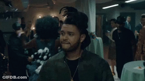 A Man Wearing A Green Jacket And A Necklace Is Standing In A Crowded Room . GIF