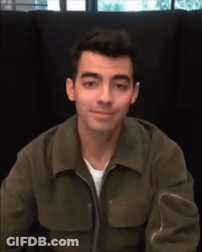 A Man Wearing A Green Jacket Is Sitting In A Chair And Smiling GIF