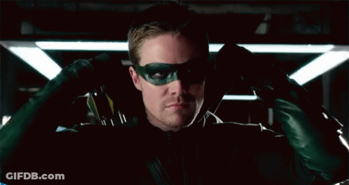 A Man Wearing A Green Mask And Gloves Is Sitting In A Dark Room . GIF