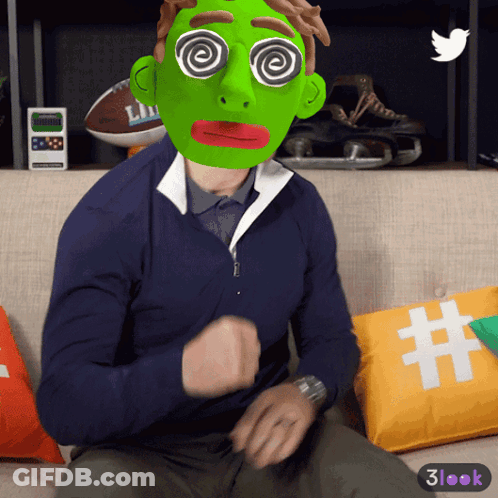 A Man Wearing A Green Mask With Hypnotic Eyes Sitting On A Couch GIF