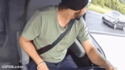 A Man Wearing A Green Shirt And A Black Hat Is Sitting In The Driver 'S Seat Of A Car GIF