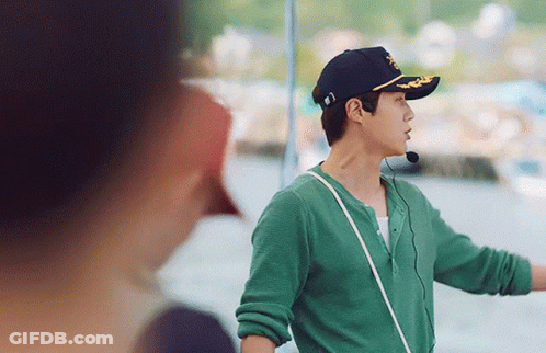 A Man Wearing A Green Shirt And A Black Hat With A Microphone Around His Neck Is Standing Next To A Woman . GIF