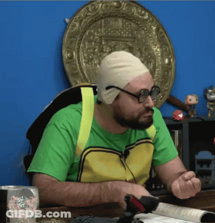 A Man Wearing A Green Shirt And A Yellow Vest Is Sitting At A Table With A Book Open . GIF