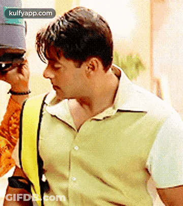 A Man Wearing A Green Shirt And A Yellow Vest Is Standing Next To A Man Wearing A Hat . GIF