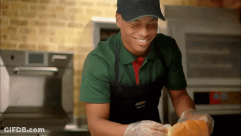 A Man Wearing A Green Shirt And Black Apron Is Smiling GIF