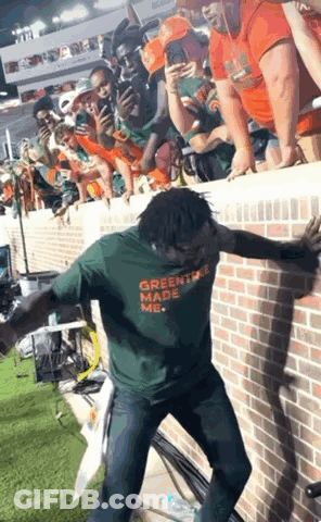 A Man Wearing A Green Shirt That Says Greentree Made Me Is Dancing In Front Of A Crowd GIF