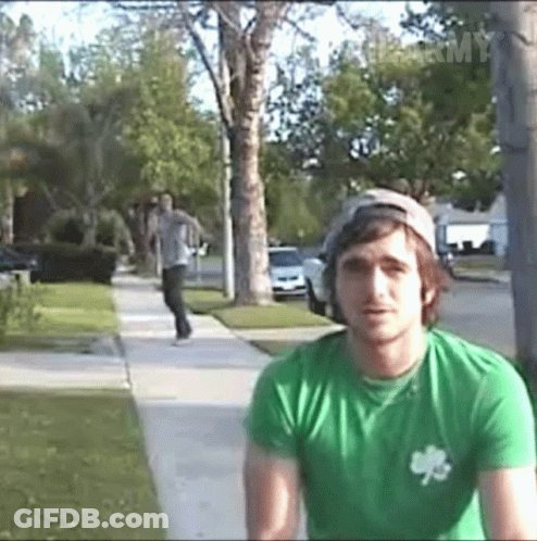 A Man Wearing A Green Shirt With A Shamrock On It Is Standing On A Sidewalk GIF