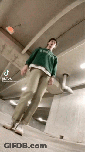 A Man Wearing A Green Sweater And Khaki Pants Is Standing In A Garage . GIF