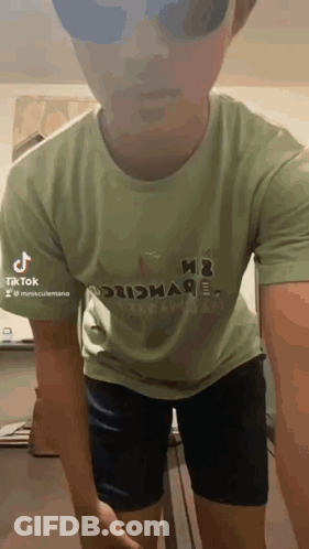 A Man Wearing A Green T-Shirt And Black Shorts Is Standing In A Room . GIF