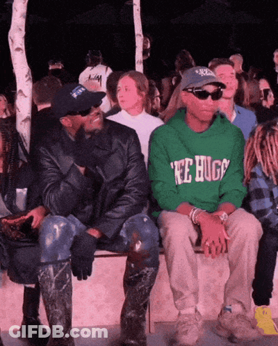 A Man Wearing A Green Tee Hugs Sweatshirt Sits Next To A Man Wearing A Black Jacket GIF
