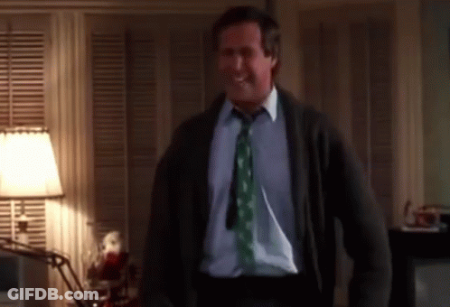 A Man Wearing A Green Tie And A Sweater Is Standing In A Room GIF