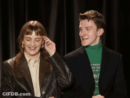 A Man Wearing A Green Turtleneck Is Standing Next To A Woman GIF