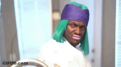 A Man Wearing A Green Wig And A Purple Hat Is Standing In Front Of A Mirror . GIF
