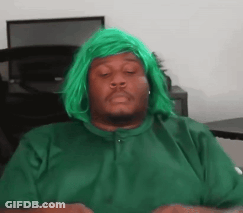 A Man Wearing A Green Wig Is Sitting At A Desk With His Eyes Closed . GIF