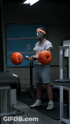 A Man Wearing A Greenfield School Shirt Is Lifting A Barbell With Pumpkins On It GIF