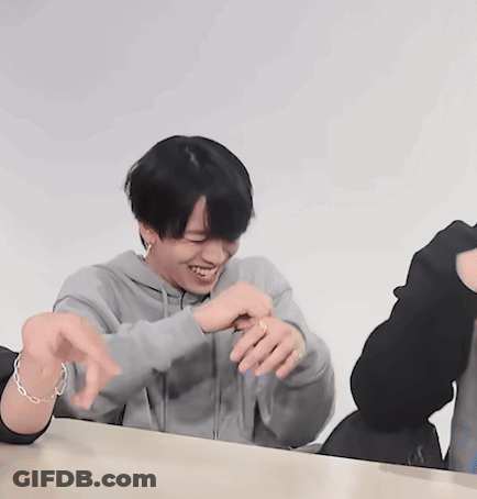 A Man Wearing A Grey Hoodie Is Sitting At A Table With His Hands Outstretched GIF