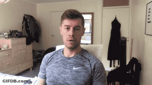 A Man Wearing A Grey Nike Shirt Is Standing In A Bedroom GIF