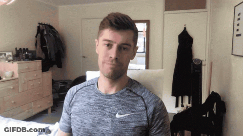 A Man Wearing A Grey Nike Shirt Stands In A Room GIF