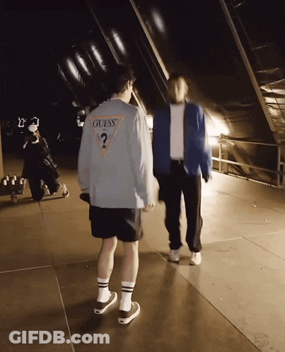 A Man Wearing A Guess Sweater Is Walking With Another Man GIF