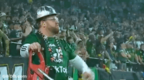 A Man Wearing A Hard Hat And A Green Shirt With The Word Kto On It Is Standing In Front Of A Crowd . GIF