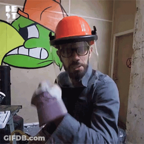 A Man Wearing A Hard Hat And Gloves Is Standing In Front Of A Wall That Has Graffiti On It GIF