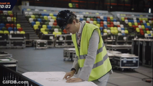 A Man Wearing A Hard Hat And Safety Vest Looks At A Piece Of Paper That Says Game In GIF