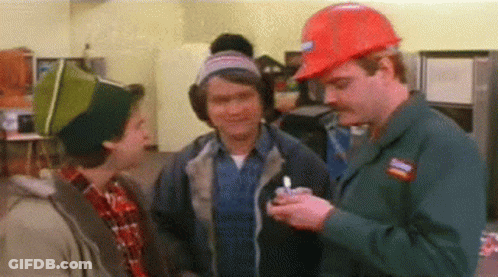 A Man Wearing A Hard Hat Is Holding A Lighter And Talking To Two Other Men In A Kitchen . GIF