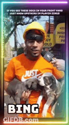 A Man Wearing A Hard Hat Is Holding Two Dogs And Talking Into A Microphone With The Word Bing On The Bottom GIF