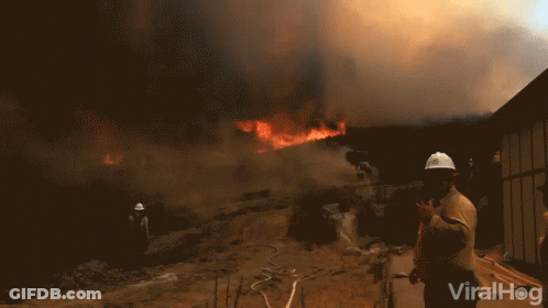 A Man Wearing A Hard Hat Stands In Front Of A Fire With The Words Viralhog Written On The Bottom GIF