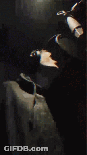 A Man Wearing A Hat And A Black Jacket Is Making A Funny Face . GIF