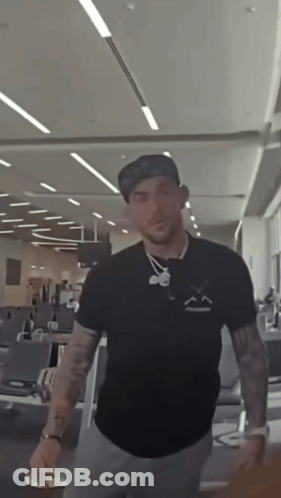 A Man Wearing A Hat And A Black Shirt With A Smiley Face On It GIF