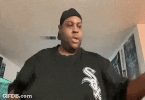 A Man Wearing A Hat And A Black Shirt With The Letter S On It Is Standing In A Living Room . GIF