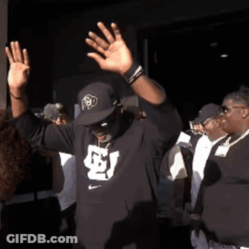 A Man Wearing A Hat And A Black Shirt With The Letter S On It GIF