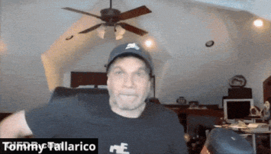 A Man Wearing A Hat And A Black Shirt With The Name Tommy Tallarico On It GIF