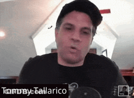 A Man Wearing A Hat And A Black Shirt With The Name Tommy Tallarico On The Bottom GIF