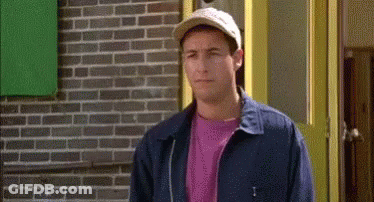 A Man Wearing A Hat And A Blue Jacket Is Standing In Front Of A Brick Building . GIF