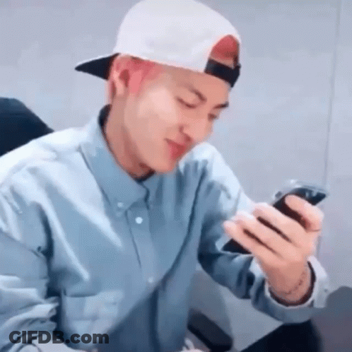A Man Wearing A Hat And A Blue Shirt Is Looking At His Phone . GIF