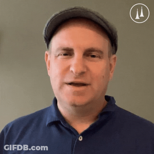 A Man Wearing A Hat And A Blue Shirt Is Looking At The Camera GIF